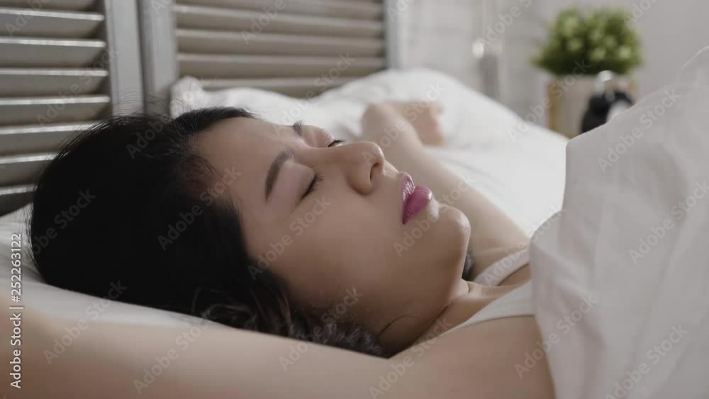 slow motion of young asian beautiful woman in tank top lying in bed cover by white quilt. lady moving head and stretching wake up in the morning in comfortable bedroom. lazy girl touching long hair slow motion of young asian beautiful woman in tank top lying in bed cover by white quilt. lady moving head and stretching wake up in the morning in comfortable bedroom. lazy girl touching long hair
