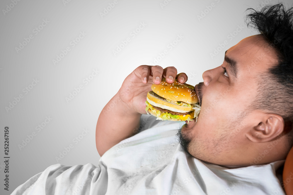 Voracious fat man eating a burger on studio Voracious fat man eating a burger on studio