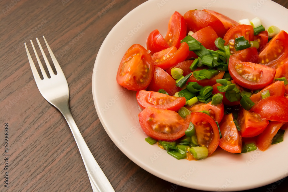 metal fork and small cherry tomatoes in a plate on a brown table