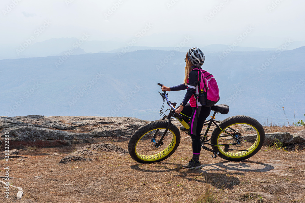 Female cyclist resting on mountain bike looking at mountain view