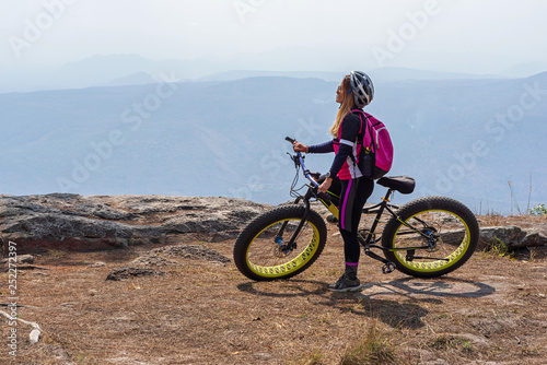 Asian female cyclist standing on mountain bike with mountain background