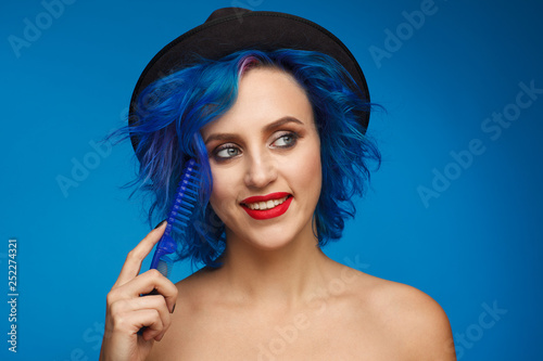 Portrait of a woman with blue hair in a black hat and with a blue hairbrush in her hand