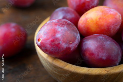 Wooden plate with ripe juicy plums on table.