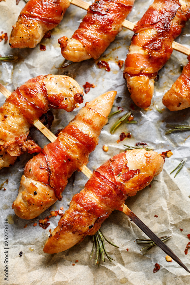 Grilled skewers of chicken tenderloin wrapped with bacon on baking paper, view from above