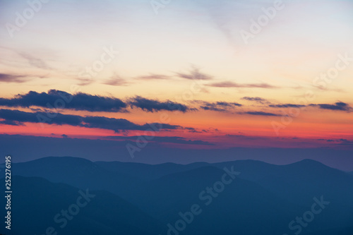 Dramatic sunset in the spring Ukrainian carpathians with red skies, rays and dark clouds, against the background of mountain ridges covered with alpine pine. © reme80