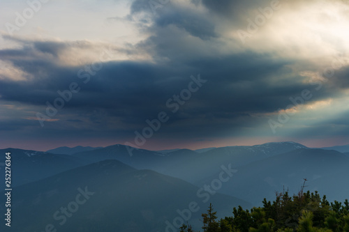 Dramatic sunset in the spring Ukrainian carpathians with red skies  rays and dark clouds  against the background of mountain ridges covered with alpine pine.
