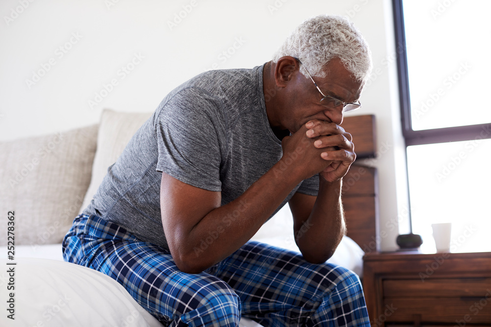 Depressed Senior Man Looking Unhappy Sitting On Side Of Bed At Home With Head In Hands Depressed Senior Man Looking Unhappy Sitting On Side Of Bed At Home With Head In Hands