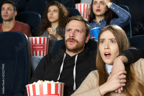Young lovely couple looking shocked while watching a movie together at the cinema