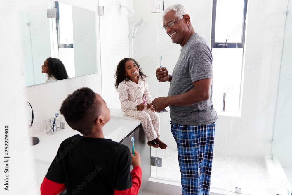 Fototapeta premium Grandfather In Bathroom Wearing Pajamas Brushing Teeth With Grandchildren