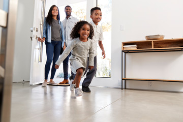 Parents And Children Returning Home Opening Front Door And Running Inside
