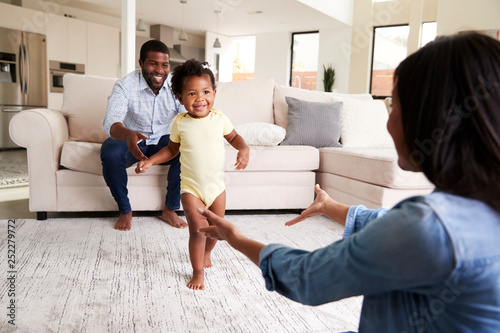 Family At Home Encouraging Baby Daughter To Take First Steps photo