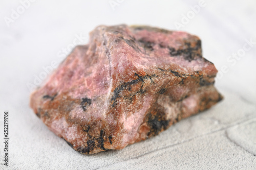 Natural mineral rock specimen - rough rhodonite stone from M. Sidelnikovo, Ural, Russia on white cement background. photo