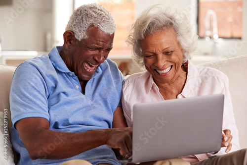 Senior Couple Sitting On Sofa At Home Together Using Laptop