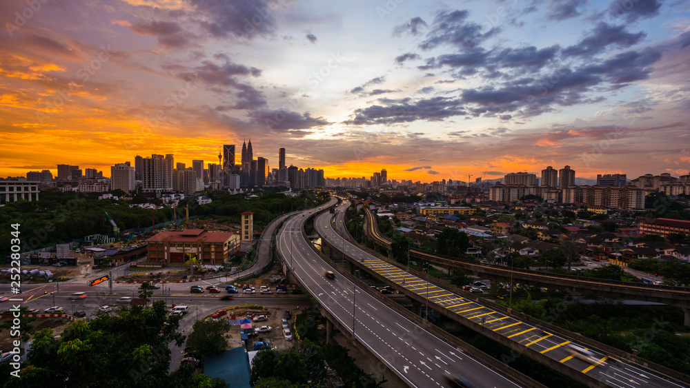 Kuala Lumpur city skyline during dramatic sunset with elevated highway leading into the city.