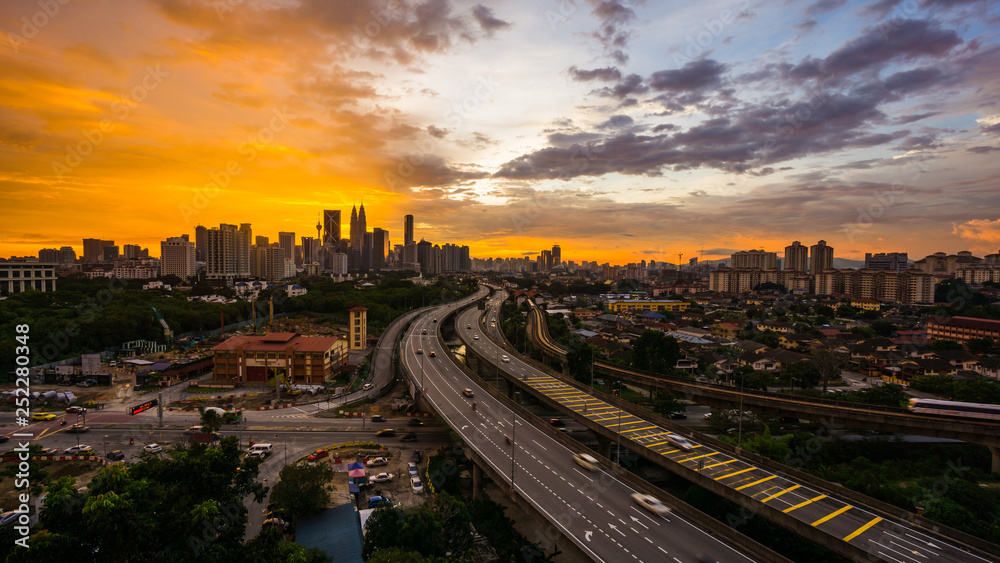 Kuala Lumpur city skyline during dramatic sunset with elevated highway leading into the city.