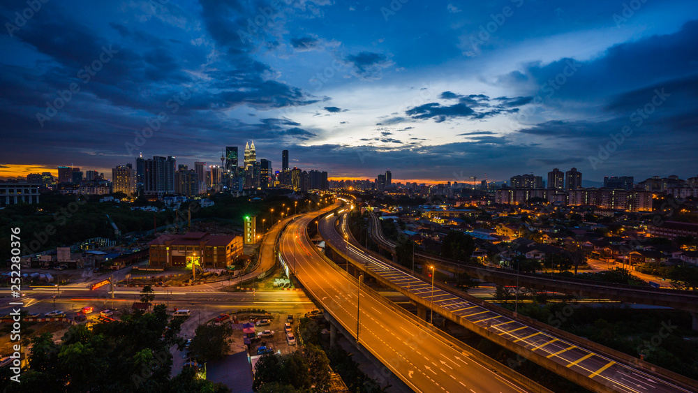 Kuala Lumpur city skyline during dramatic sunset with elevated highway leading into the city.