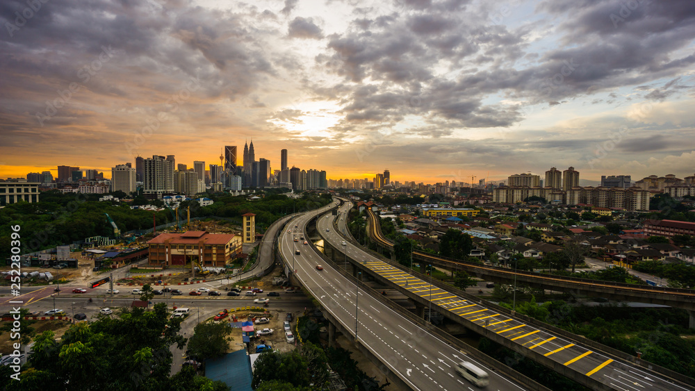 Kuala Lumpur city skyline during dramatic sunset with elevated highway leading into the city.