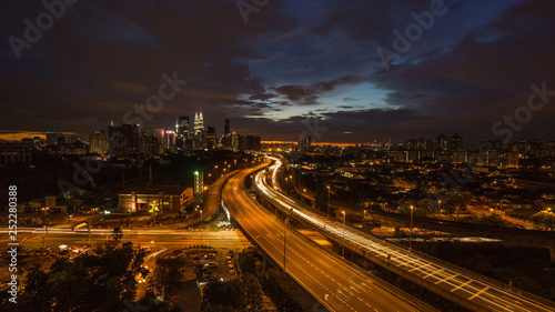 Kuala Lumpur city skyline during dramatic sunset with elevated highway leading into the city.