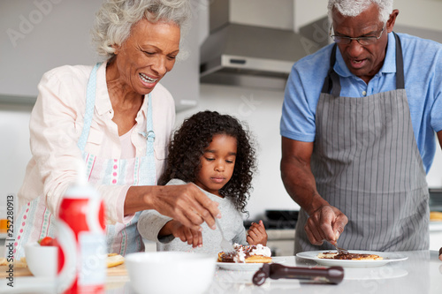 Grandparents In Kitchen With Granddaughter Making Pancakes Together