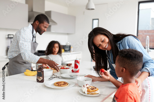 Family In Kitchen At Home Making Pancakes Together