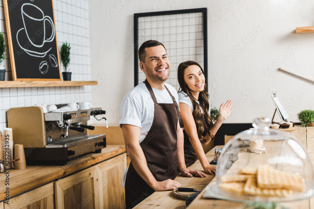 cashiers in aprons standing and smiling behind bar counter in coffee house cashiers in aprons standing and smiling behind bar counter in coffee house