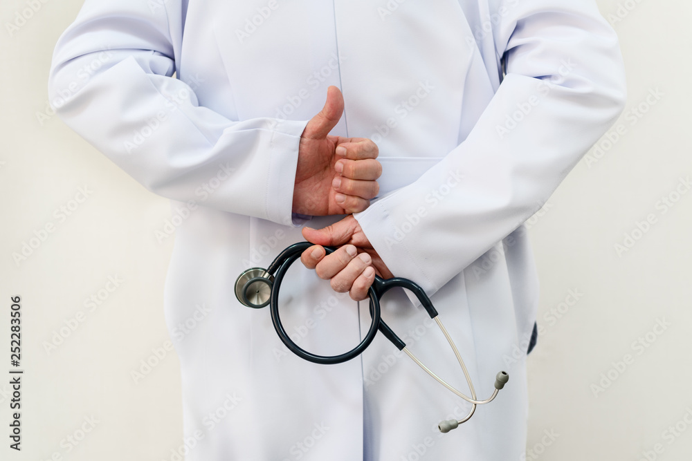 white coat dressing male holding stethoscope in right hand and thumb up left hand behind the back white coat dressing male holding stethoscope in right hand and thumb up left hand behind the back