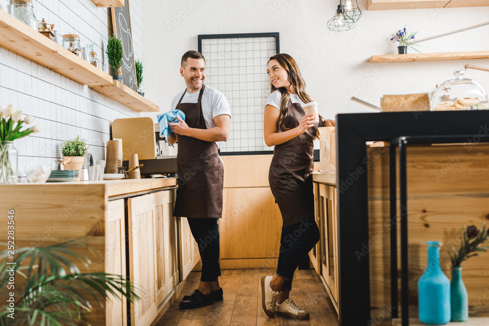 barista and cashier standing behind bar counter in coffee house