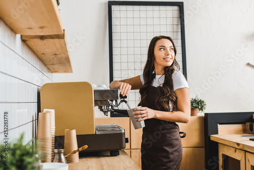 Fotografie attractive brunette barista holding cup and making coffee with machine in coffee