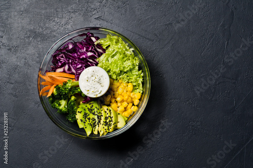 Buddha bowl, healthy and balanced food. Ingredients broccoli, corn, carrots, couscous, lettuce, cabbage, sauce. Black background, top view, space for text