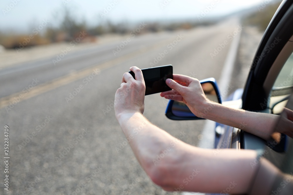 Man taking photos of desert landscape out of car window on remote highway