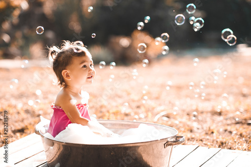 Cute bby girl 1-2 year old having bath with soap bubbles outdoors close up. Summer time. Childhood.