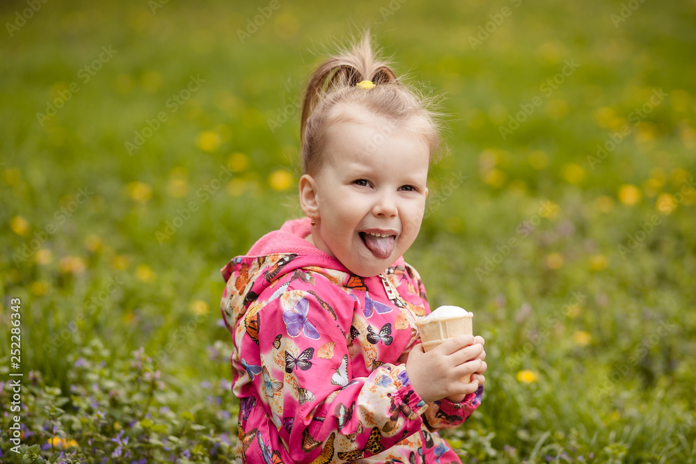 A small cute girl of 3-4 years old is sitting on the grass in early spring and eating a delicious ice cream in a waffle cup. The girl got dirty and dirty. A small cute girl of 3-4 years old is sitting on the grass in early spring and eating a delicious ice cream in a waffle cup. The girl got dirty and dirty.