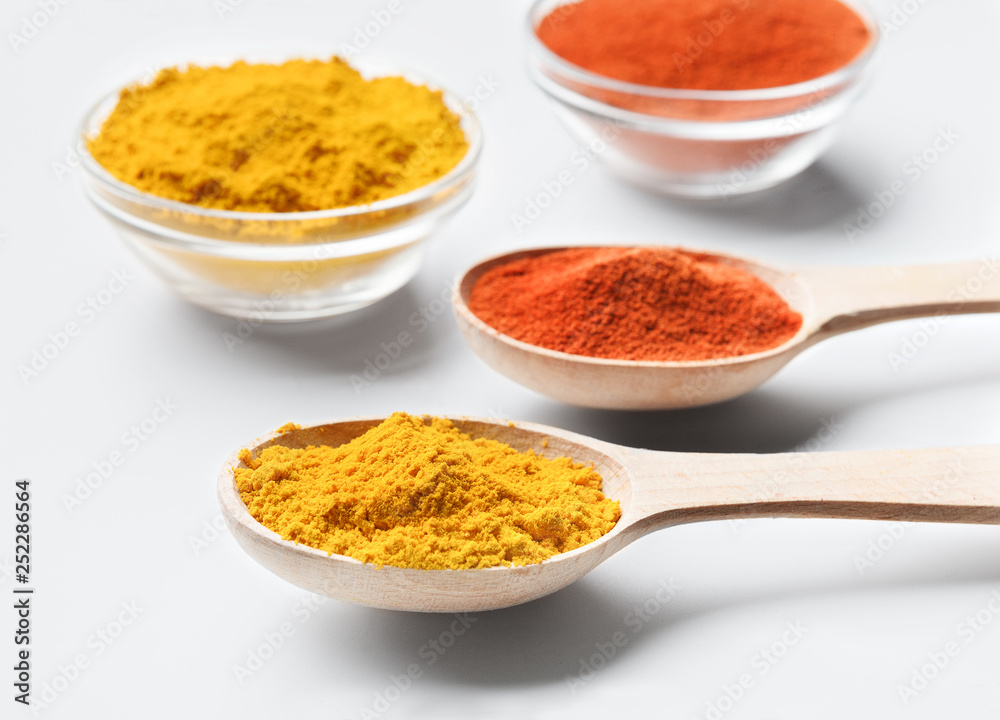 Wooden spoons and bowls with paprika and turmeric powder on white Wooden spoons and bowls with paprika and turmeric powder on white