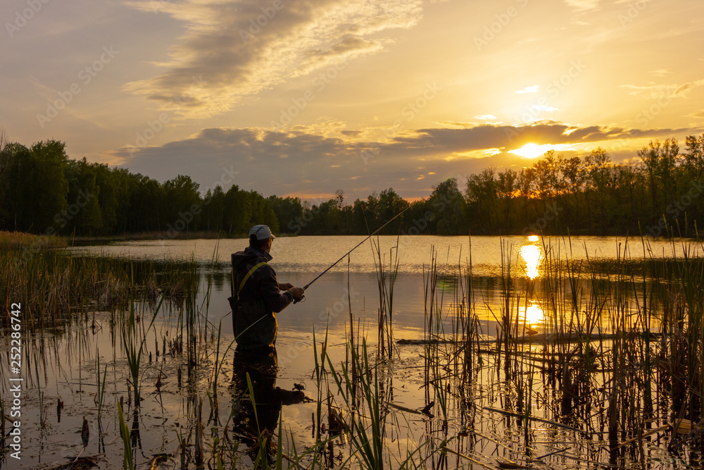 angler standing in a lake and catching the fish at sunset