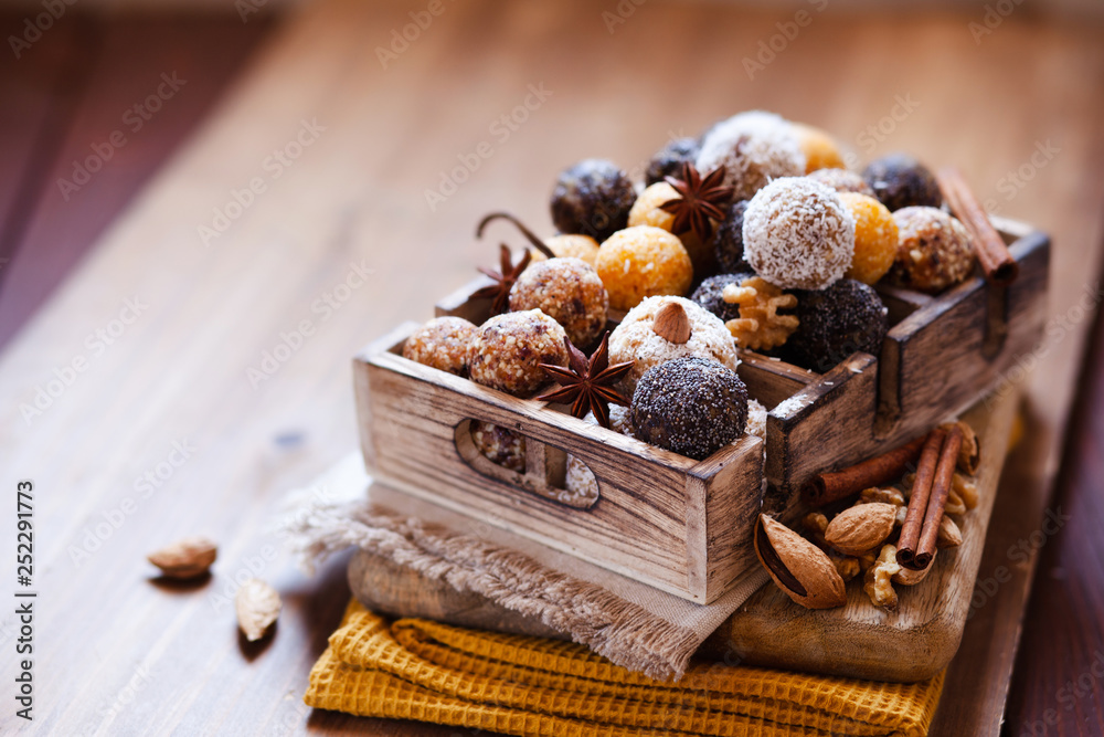 Vegan organic energy bites with nuts, chia, dates, coconut and dried fruits, healthy raw dessert snacks on wooden table