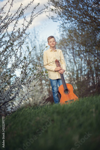 Portrait of a young teen standing in spring park and playing guitar.