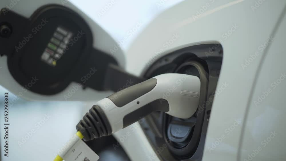 Plug in electric power to the car. New era of vehicle fuel. Power charging of white modern electric automobile. Urban electric car plugged into an electric vehicle charging station. Plug in electric power to the car. New era of vehicle fuel. Power charging of white modern electric automobile. Urban electric car plugged into an electric vehicle charging station.