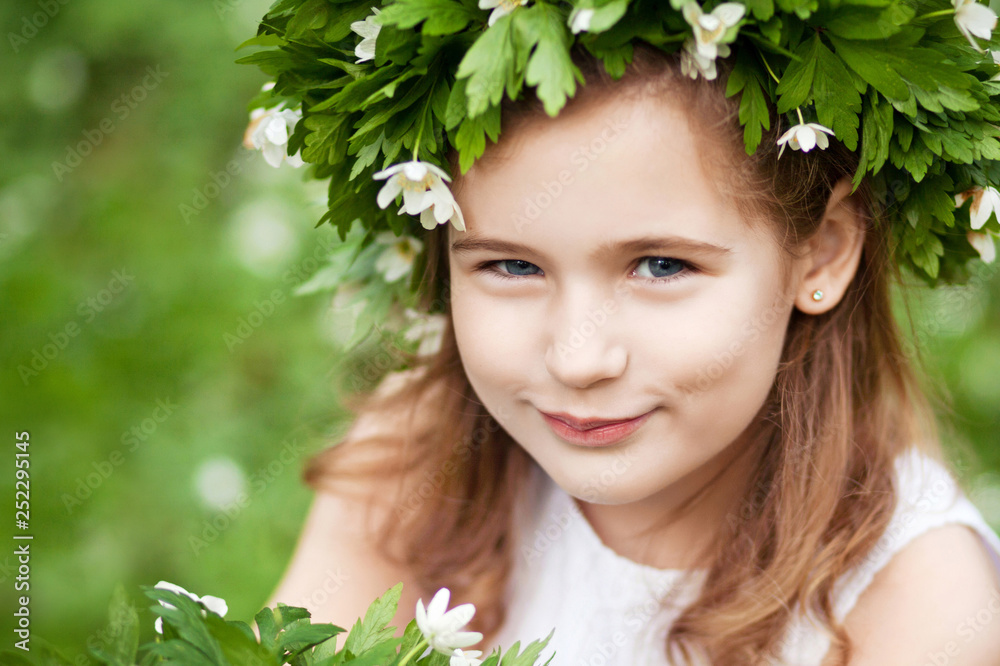 Beautiful little girl in a white dress in the spring wood. Portrait of the pretty little girl with a wreath from spring flowers on the head. Easter time Beautiful little girl in a white dress in the spring wood. Portrait of the pretty little girl with a wreath from spring flowers on the head. Easter time