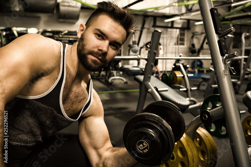Handsome young athletic man lifting weights at the gym studio