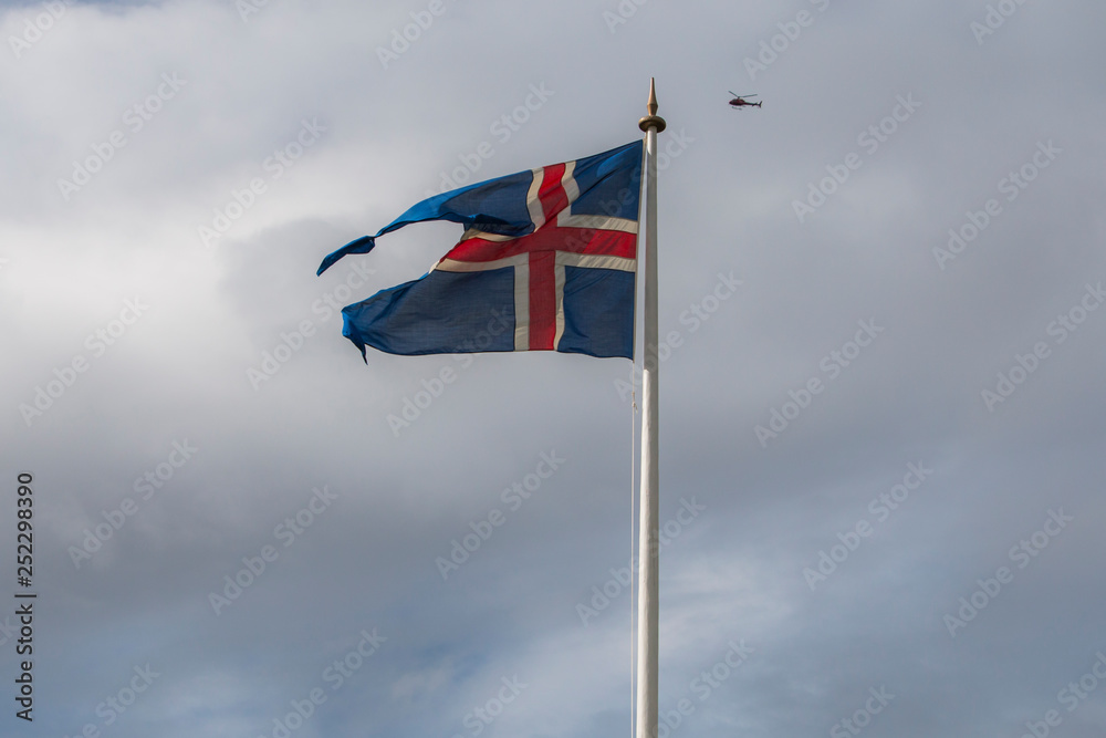 Icleandic flag in cloudy sky, helicopter flying in background