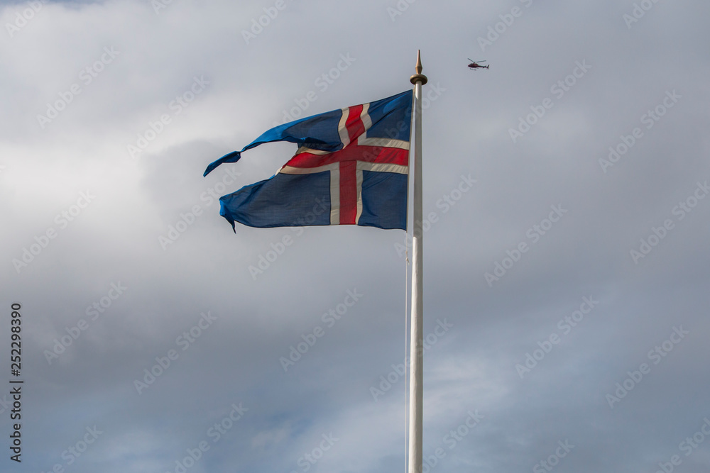 Icleandic flag in cloudy sky, helicopter flying in background Icleandic flag in cloudy sky, helicopter flying in background