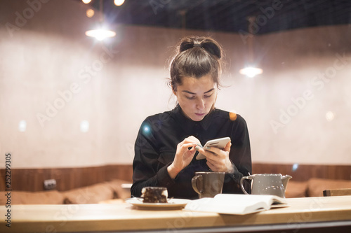 An attractive girl sits in front of a panoramic window at the cafe, drinking coffee and eating dessert. selective focus, noise effect