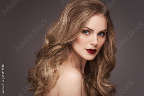 Young brown-haired woman with long curly hair. Beautiful face of gorgeous girl with blue eyes. Nice portrait of a caucasian female looking at camera. Attractive fashion model