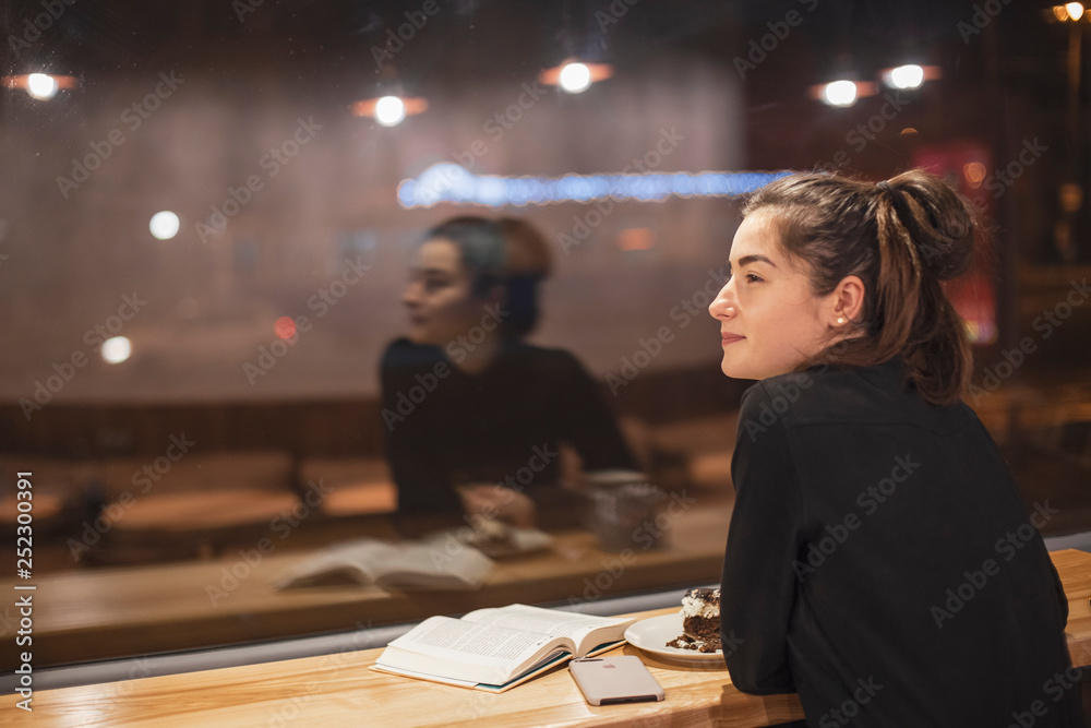 Gorgeous smiling young woman with dark hair eating cake and drinking coffee at a cafeteria in the evening sitting by the window. selective focus, noise effect Gorgeous smiling young woman with dark hair eating cake and drinking coffee at a cafeteria in the evening sitting by the window. selective focus, noise effect
