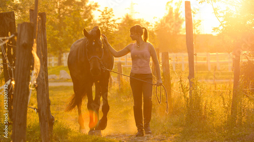 SUN FLARE: Cheerful girl walking down the grassy trail with her beautiful horse.