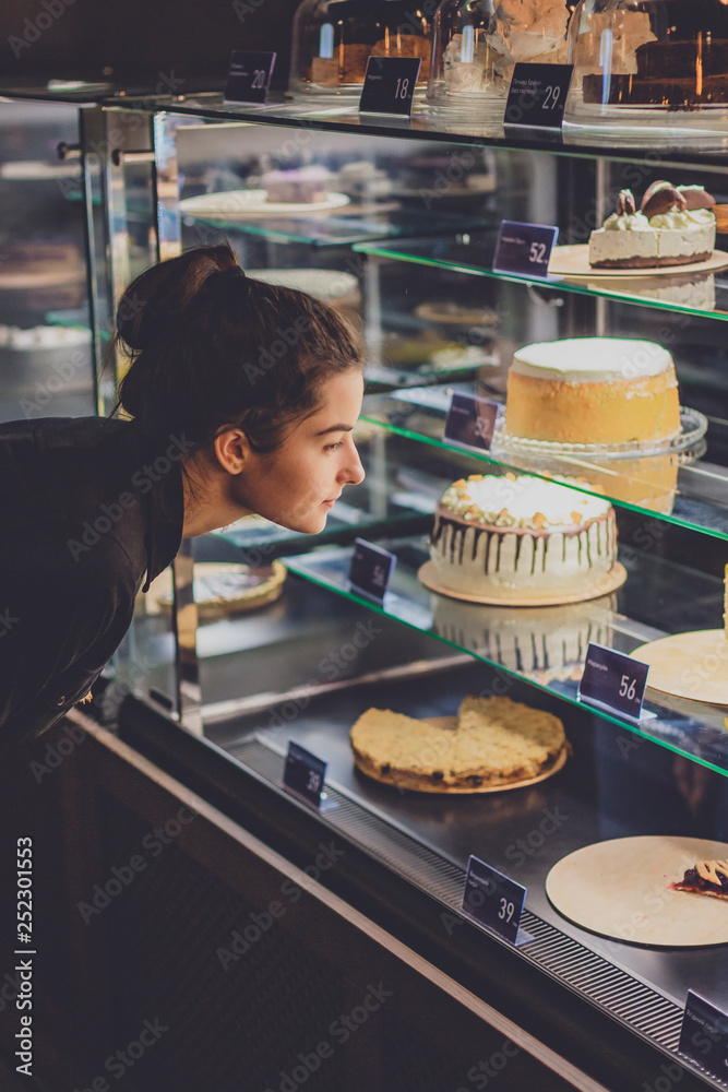 In pastry shop girl choose colorful cake and pie from showcase. selective focus, noise effect
