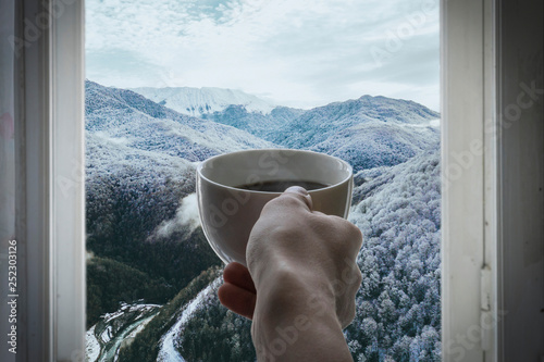 persons hands hold cup of hot coffe opposite from the window at winter season b photo