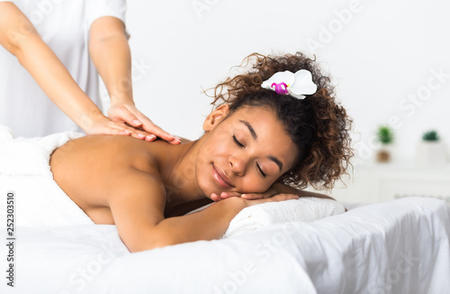African-american girl enjoying back massage in spa salon