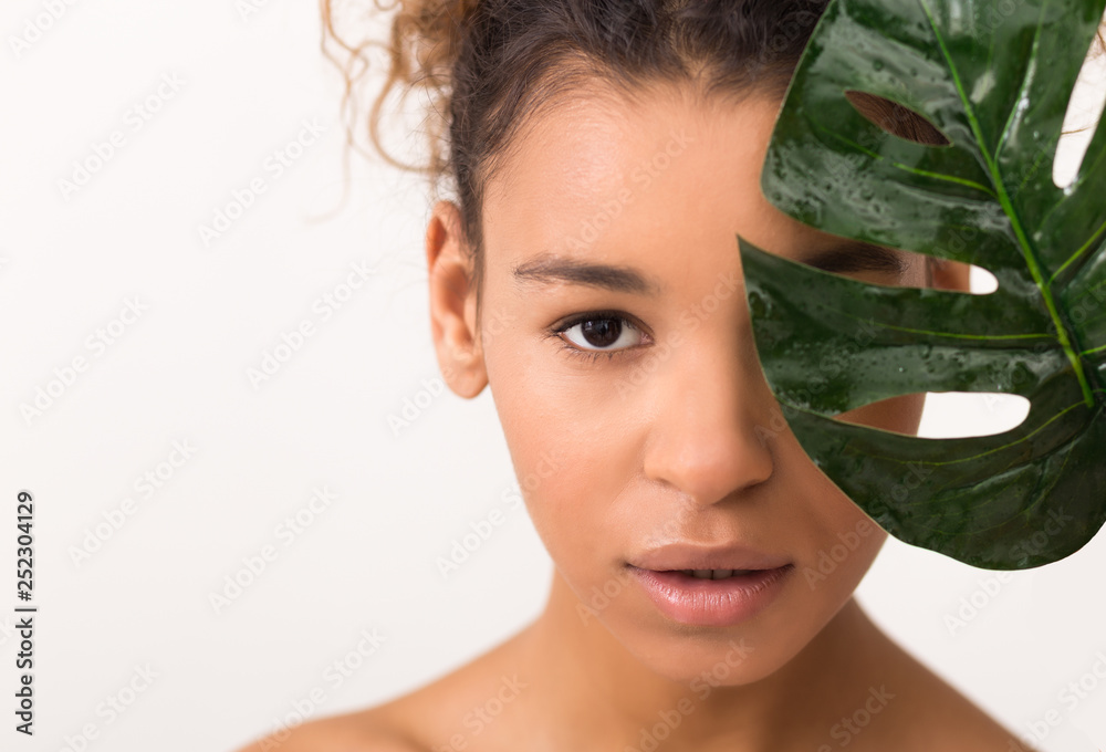 African-american woman with green tropical leaf, light background African-american woman with green tropical leaf, light background