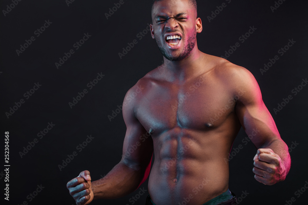 Attractive African male fighter or boxer posing shirtless, isolated over dark background. Toned and ripped muscular fitness man under dramatic low key lighting, copy space.